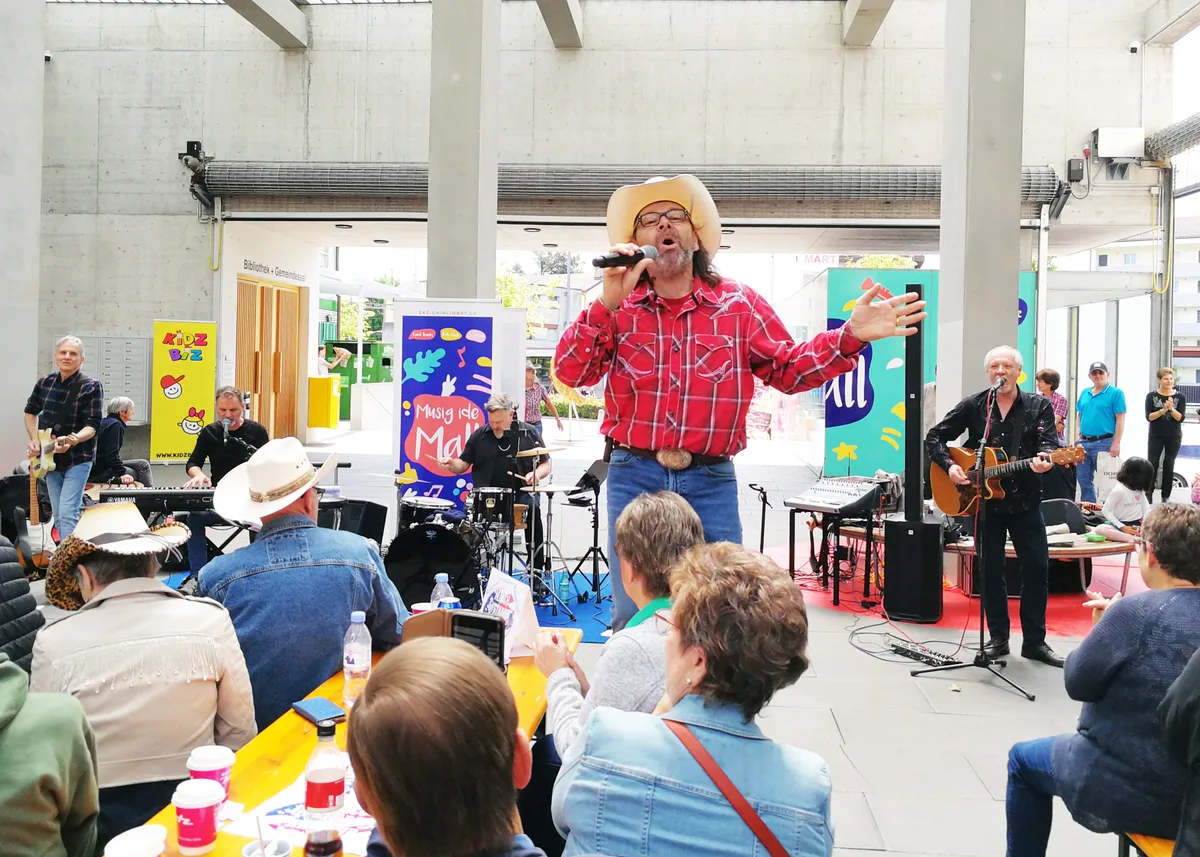 Fehlt die Bühne, tut es auch mal eine Festbankgarnitur. Viele Menschen sitzen auf Festbänken, ein Mann mit Cowboyhut steht dazwischen und singt.